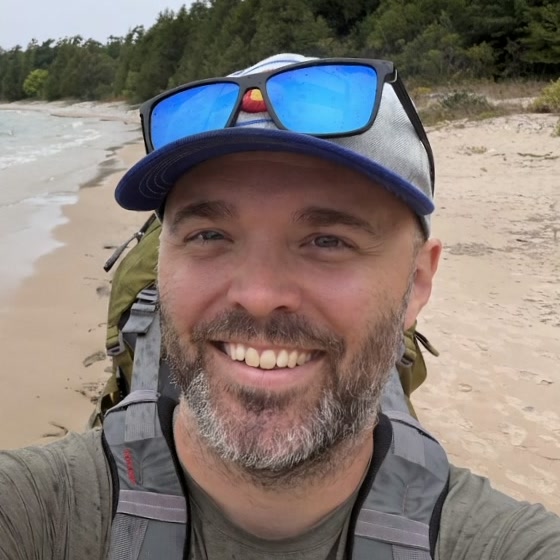 Drew Mooney smiling on a beach, sunglasses on his cap